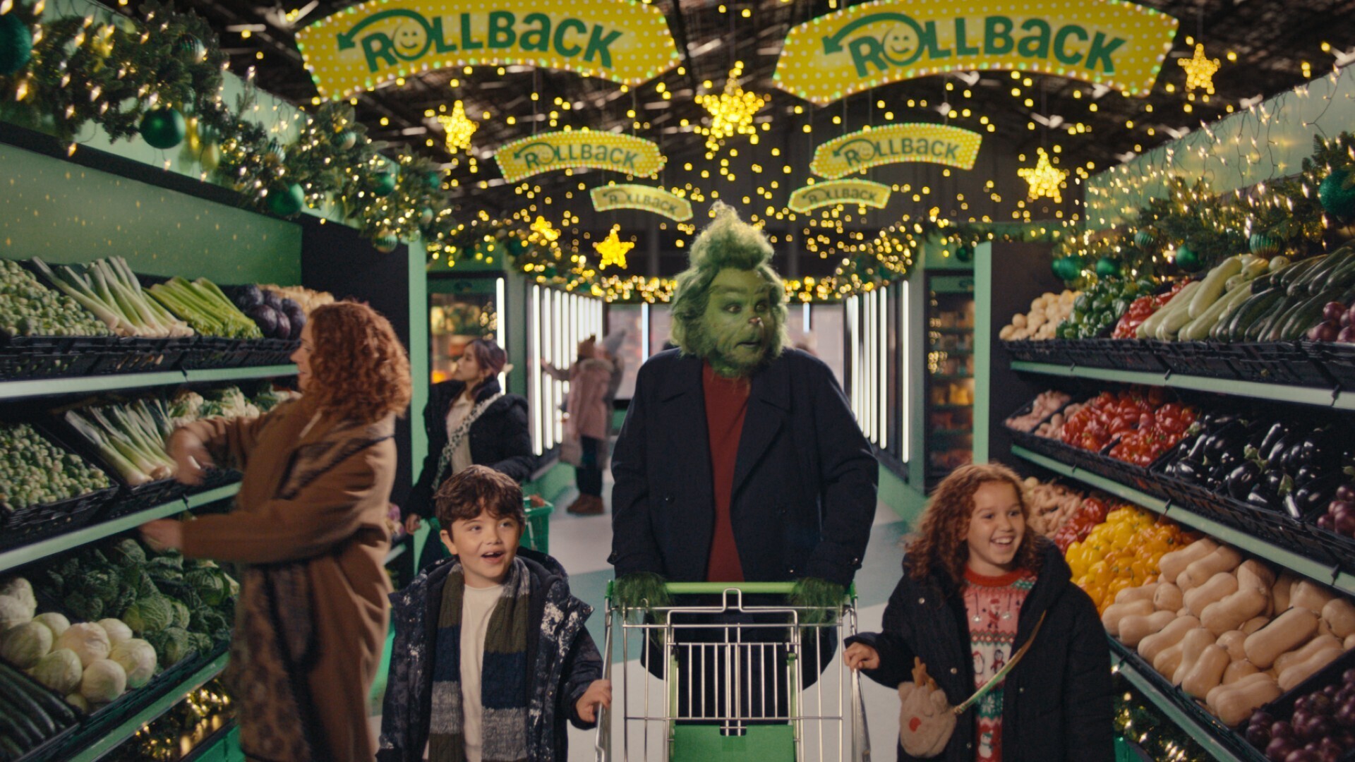 Still image of the Grinch walking through Asda during Christmas with his family, pushing a shopping carriage  