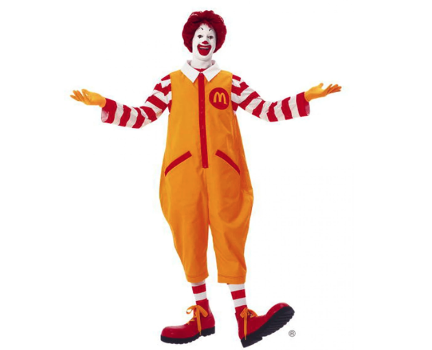 A clown, with red hair, a white painted face, and yellow overalls with a red and white striped shirt, yellow gloves, and very large red shoes with yellow laces 