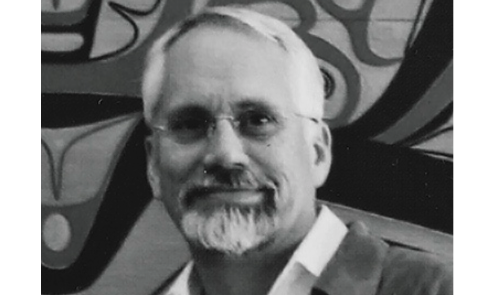 Dan Wieden looks into the camera against a graffitied background. 