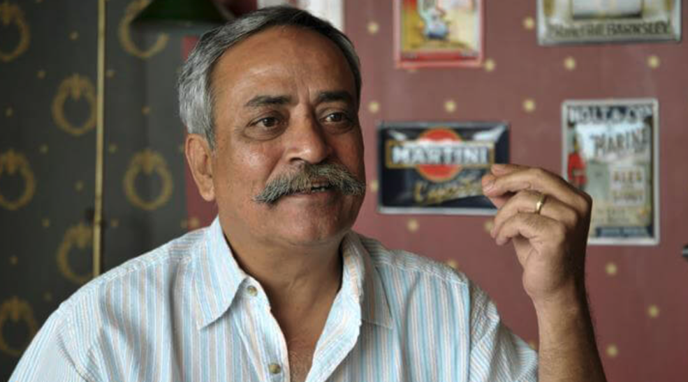 Piyush Pandey sits in front of a wall of vintage ad prints, gesturing with his hand as he talks. 