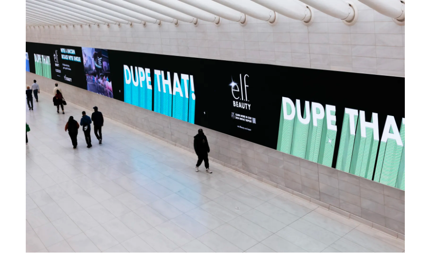 Photo of a hallway, taken from a high angle, showing an advertisement from e.l.f. Cosmetics along the wall. The words “Dupe That!” in blue and green are interspersed with images. 