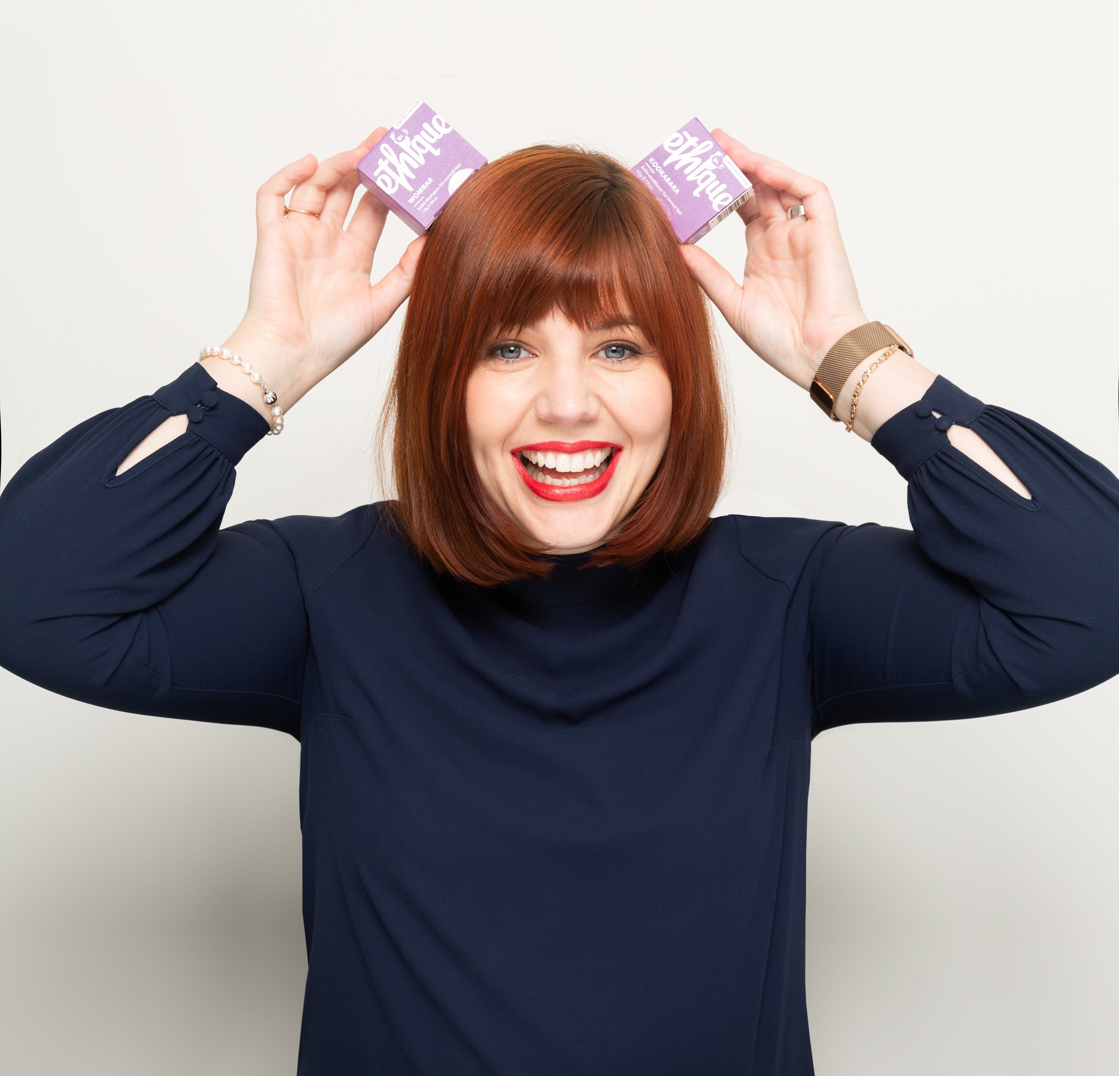 Ethique founder poses in front of white background holding up two boxes of solid beauty bars