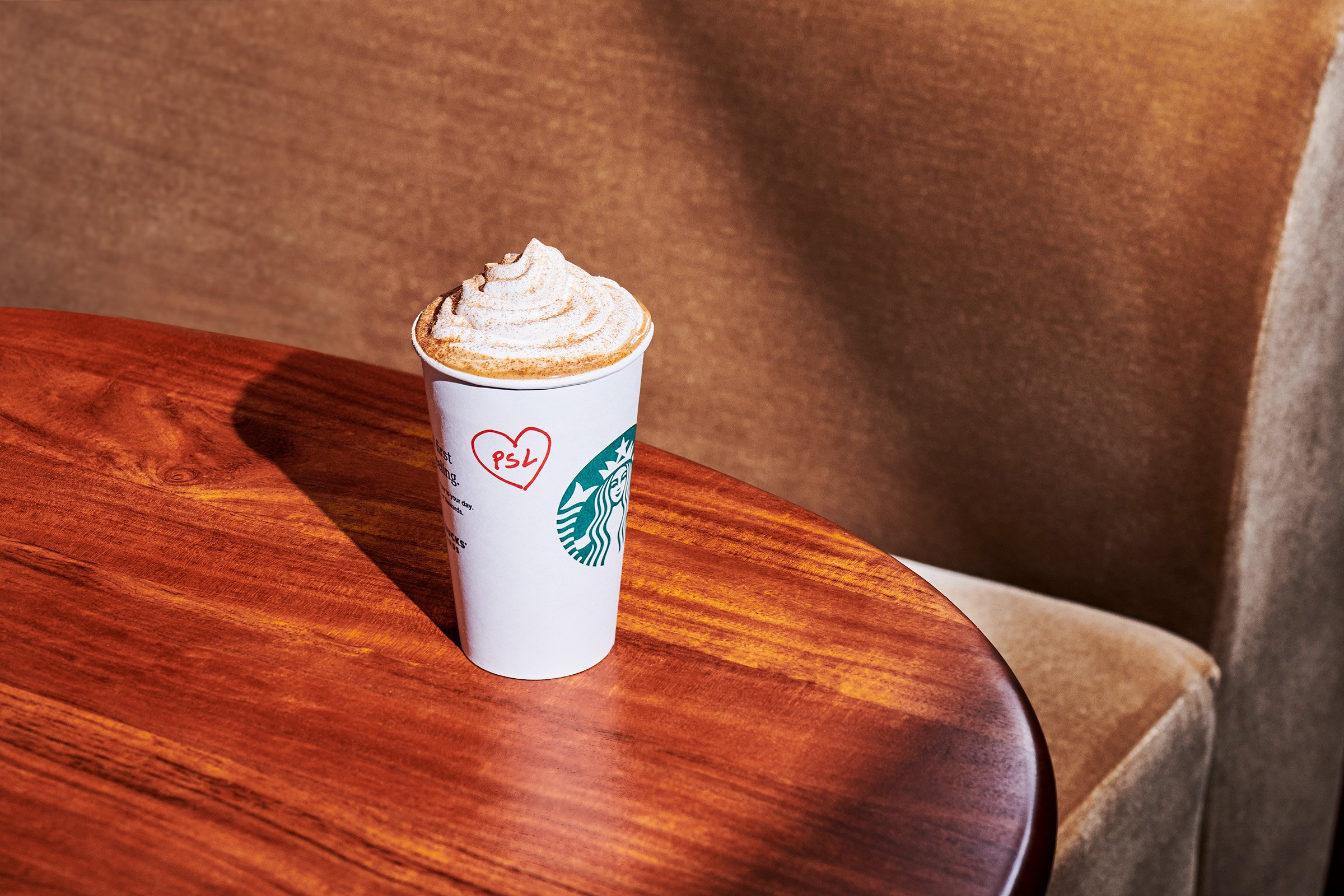 Starbucks' Pumpkin Spice Latte PSL on a wooden table topped with whipped cream with a red heart around the letters 